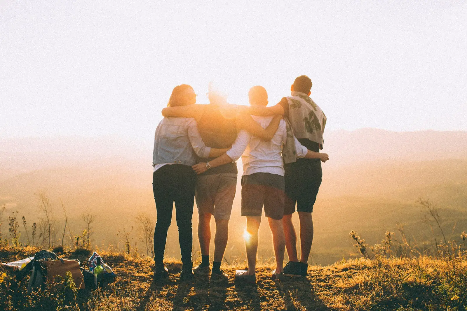 Friends arm in arm on a hilltop at sunrise